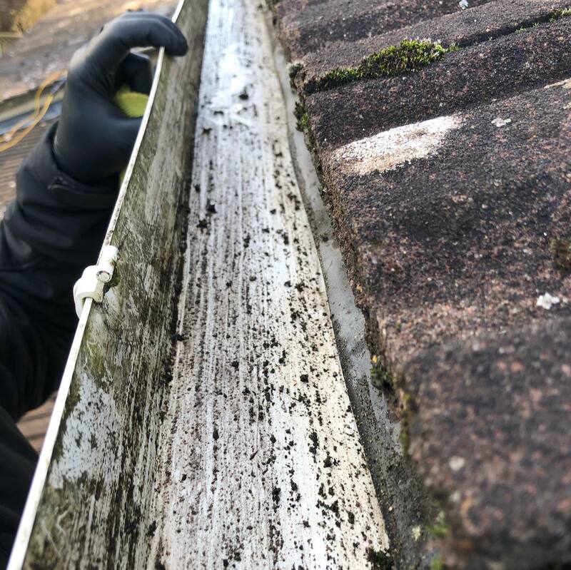 Gloved hand cleaning a metal gutter